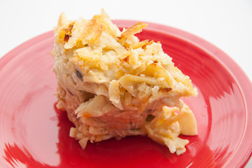 Tuna noodle casserole closeup cut and ready to eat on a red plate.  This piece of casserole has peas in it and potato chips on top.