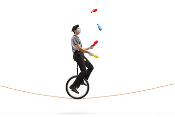 Mime riding a mono-cycle on a rope and juggling