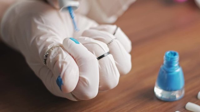 A young girl paints nails on a glove with blue varnish. Female hands in white latex gloves in the rings. Security and beauty during the quarantine period. Close up.