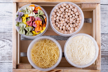 Chickpeas, pasta and corn flour in plastic jars in the wooden box. Top view