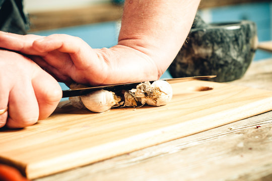 male hands crush garlic on a kitchen board