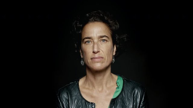 Close up of a mature woman with short hair staring at camera.  Mid adult woman wearing a jacket isolated on black background.

