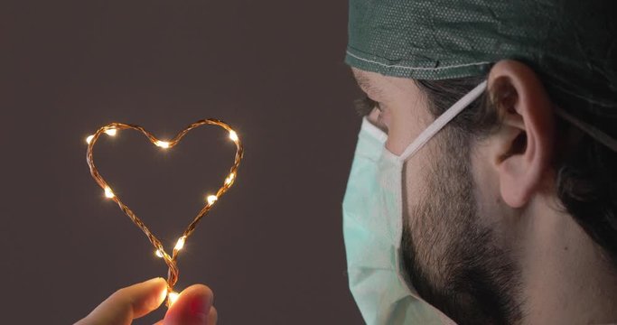 Occhi in primo piano di un medico in prima linea alla lotta al Coronavirus tiene in mano un piccolo simbolo del cuore luminoso per dare speranza alla fine della pandemia Coroanvirus.