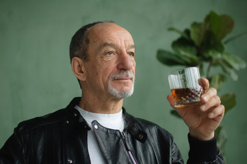 Side view of senior man holding glass of whisky or brandy and thinking about something in loft...
