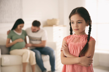 Unhappy little girl and her father with pregnant mother at home. Feeling jealous towards unborn sibling