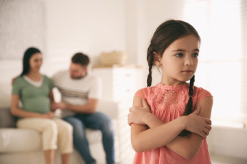 Unhappy little girl and her father with pregnant mother at home. Feeling jealous towards unborn sibling