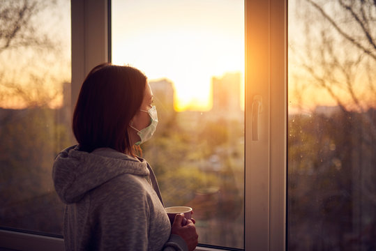 Woman near window at sunset in isolation at home for virus outbreak. Stay home concept