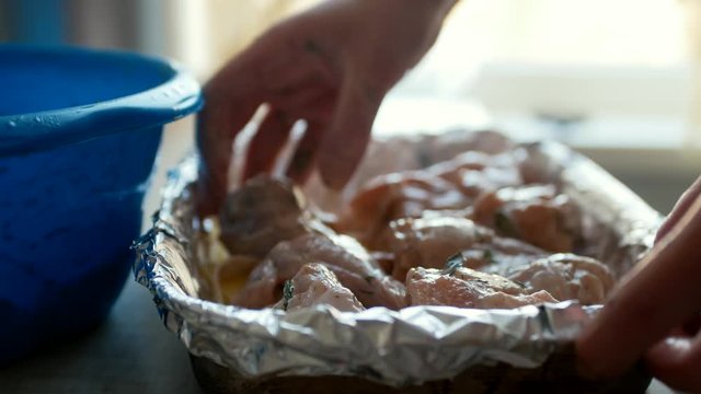 Сlose-up. A young housewife puts chicken legs on potatoes on a foil in a baking sheet. Homemade chicken meat in potato sauce.