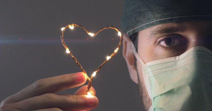 Sguardo con occhi in primo piano di un giovane medico chirurgo mentre tiene in mano il simbolo del cuore per dare speranza ai malati di covid-19. Concetto di coronavirus.