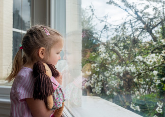 While epidemic of coronavirus people are required to stay at home and avoid social contacts. Little girl stays in self-isolation despite good spring weather.