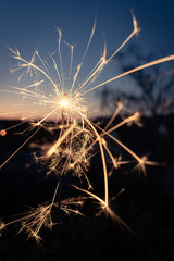 The last rays of a burning sparkler at dusk against a small-town background; blurred