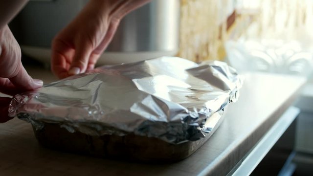 Сlose-up. A young housewife foils chicken legs with potatoes in sauce. Cooking a dish for immersion in the oven.