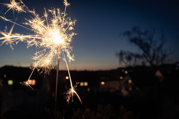 Burning sparkler as a symbol of a new beginning above the roofs of a small town in the evening; blurred background