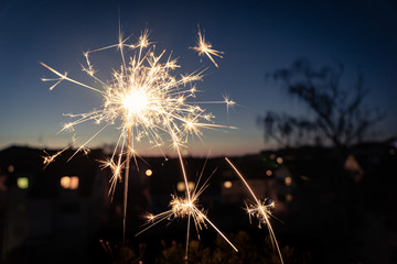 Burning sparkler in the evening with a touch of New Year's Eve over the roofs of a small town; blurred background