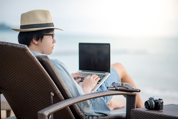 Asian freelance man in casual clothing using laptop computer on beach chair looking at the sea....