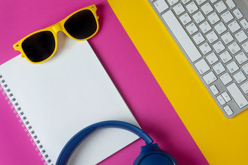 Flat lay composition with headphones, sunglasses, notepad and keyboard on a yellow purple background. Webinar or podcast concept.