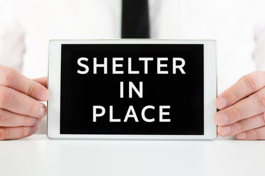 Businessman Holding A Smart Tablet With Sign Shelter In Place On Screen, Encouraging People To Stay Home