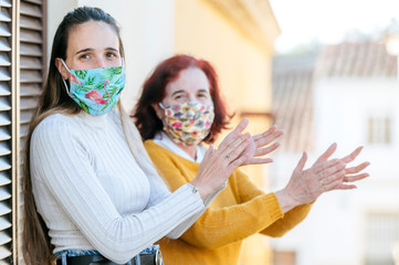 Two women with face mask clapping on the balcony - Powered by Adobe