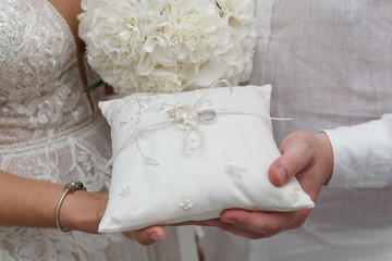 two gold wedding rings on a white pillow in the hands of newlyweds. bride and groom holding wedding rings in hands close up. wedding day and details.