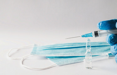 Healthcare worker with gloves holding a syringe, ampoule and masks on a white background. Blurred...