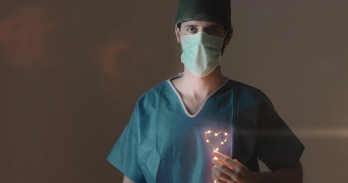 Occhi in primo piano di un medico in prima linea alla lotta al Coronavirus tiene in mano un piccolo simbolo del cuore luminoso per dare speranza alla fine della pandemia Coroanvirus.