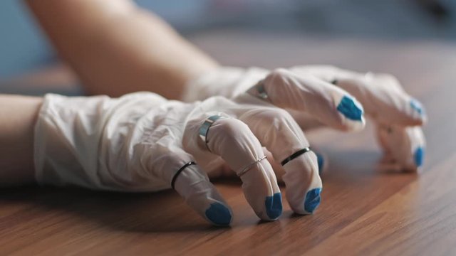 Hands of young woman in white latex gloves in rings with painted blue nails tapping her fingers on the table waiting or thinking something. Concept of safety and beauty during a pandemic. Close up.