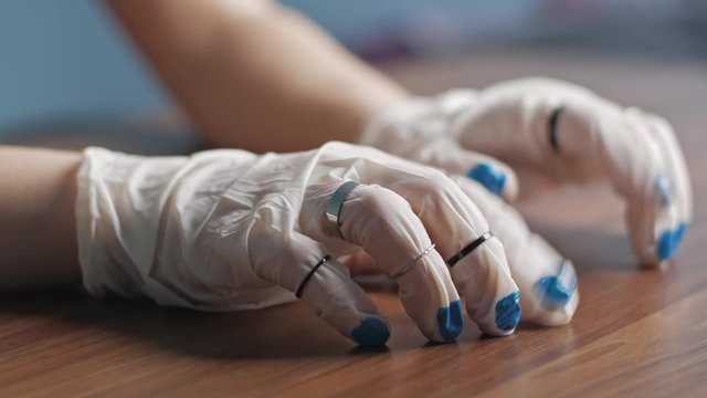 Hands of young woman in white latex gloves in rings with painted blue nails tapping her fingers on the table waiting or thinking something. Concept of safety and beauty during a pandemic. Close up.
