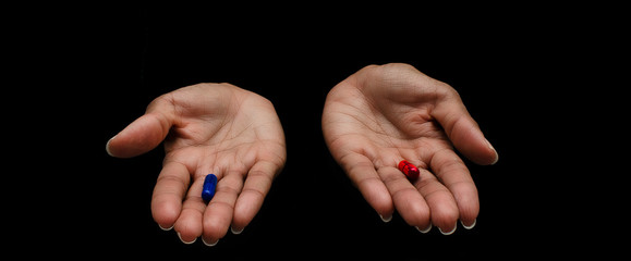 Hands of a black woman offering the red and the blue pills on a black background.  Concept of ugly...