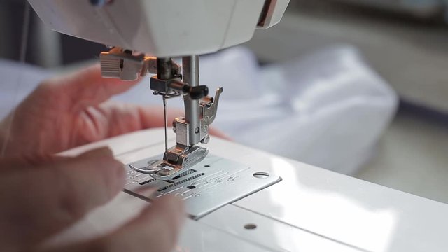 seamstress woman tries to thread a white thread into the needle of a sewing machine and she does not succeed and she shrugs her hands close-up