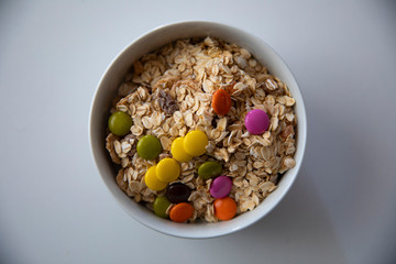 a bowl of corn flakes and colourful bonbons on white background
