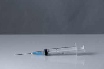 A medical syringe with a needle stands on a white table on a gray background. photo for design or advertising