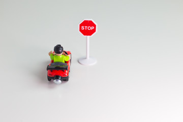 Coche de juguete parado ante una señal de trafico de STOP. Sobre fondo blanco.
