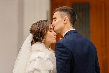 Groom elegantly kisses the bride on the forehead. Wedding photography of stylish newlyweds. Close-up portrait.