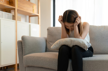 Depression and sadness concept,Young asian woman covering her face sitting on sofa in home.