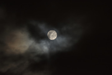 the dark but thinning clouds of a rain storm pass by the full moon