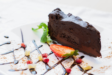 Dark cheesecake decorated with strawberries and mint on a white plate