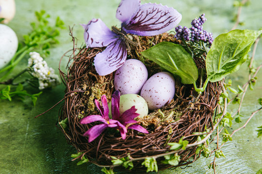 Happy easter concept. Multicolored easter painted eggs in the nest, flowers and branches with buds on a green background.