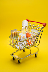 Miniature shopping trolley with medicines, antiseptic. Self-isolation. Yellow background.