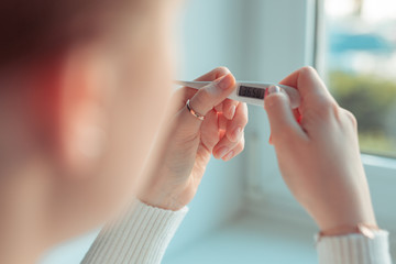 European woman checking high temperature with thermometer. Corona virus infection symptoms headache...