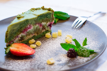 sweet pistachio cake on a dark plate with candied mint leaves and strawberries