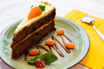 Delicate slice of carrot cake with marmalades on a green plate on a background of a yellow napkin with a spoon