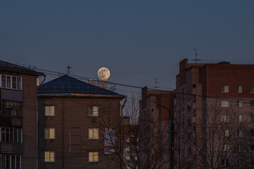 a huge full moon travels through the sky against the backdrop of urban houses