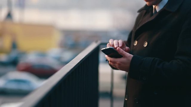 Businessman in a black coat standing on the street surfing in a smartphone on the phone