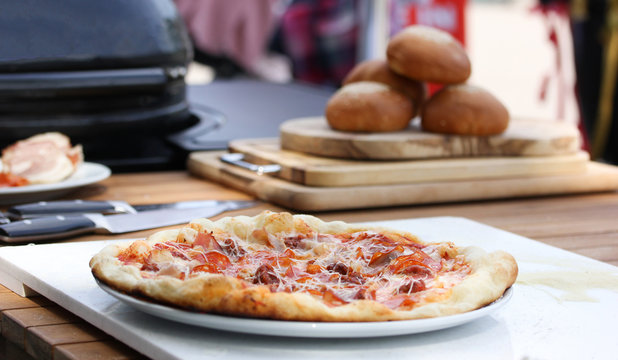Italian cuisine. Pizza with hands of chef from the grill. Dough, ketchup, bacon, salami, sausage and cheese on a white board on a wooden table. Background image, copy space
