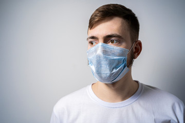 A young man in a medical mask on a white background looks away. Self isolation