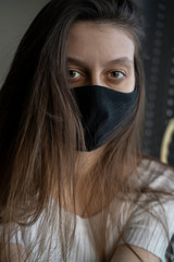 A girl in a black medical mask looks at the camera. Loose hair. Self isolation