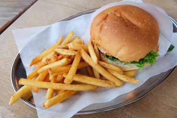 Burger and french fries on parchment paper, on tin dish, on wooden table in cafe, close-up. Concept cheatmeal, malnutrition, junk food, delivery. Horizontal, side view