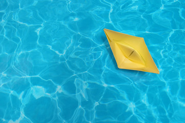 The little yellow paper ship on the blue water surface. Minimal concept summer and travel flat lay, copy space for mock-up
