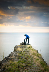 Male person is cuddling dog in nature in front of the sea with dramatic sky in the background....