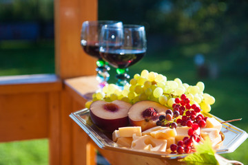 Two glasses of red wine and cheese board, fresh grapes, peaches and berries on wooden table.